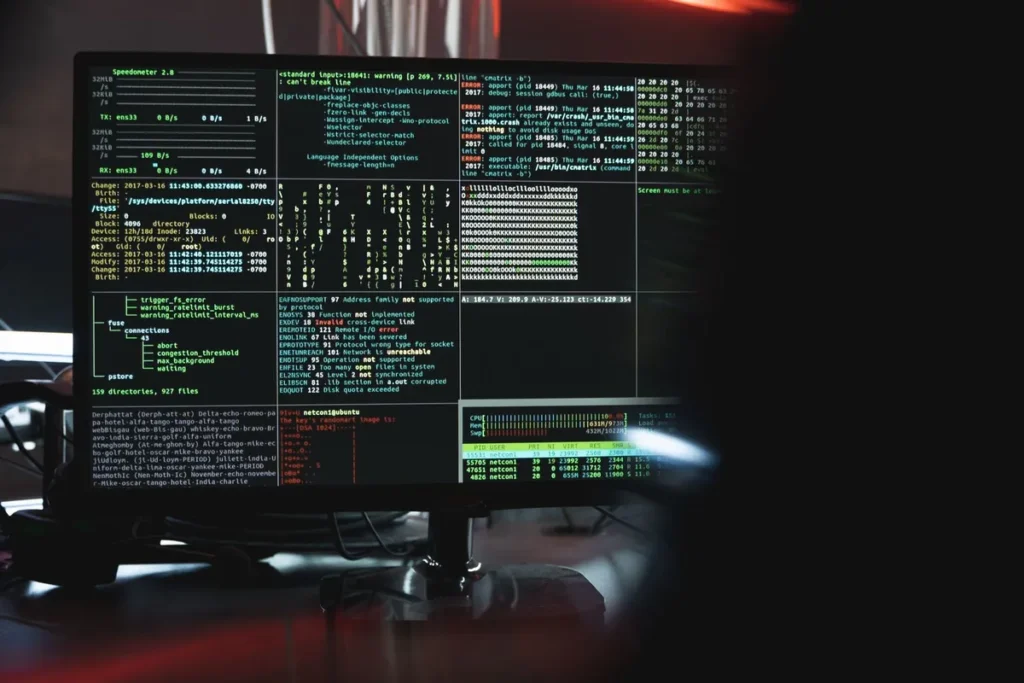Computer monitor showing terminal windows full of code in a dark room