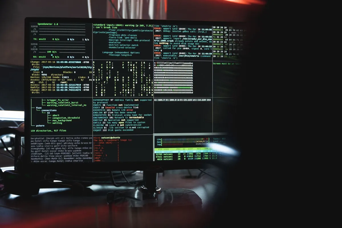 Computer monitor showing terminal windows full of code in a dark room